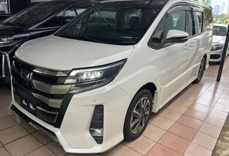 White Toyota Voxy minivan with sliding doors parked in showroom, perfect family vehicle for KK car rental services